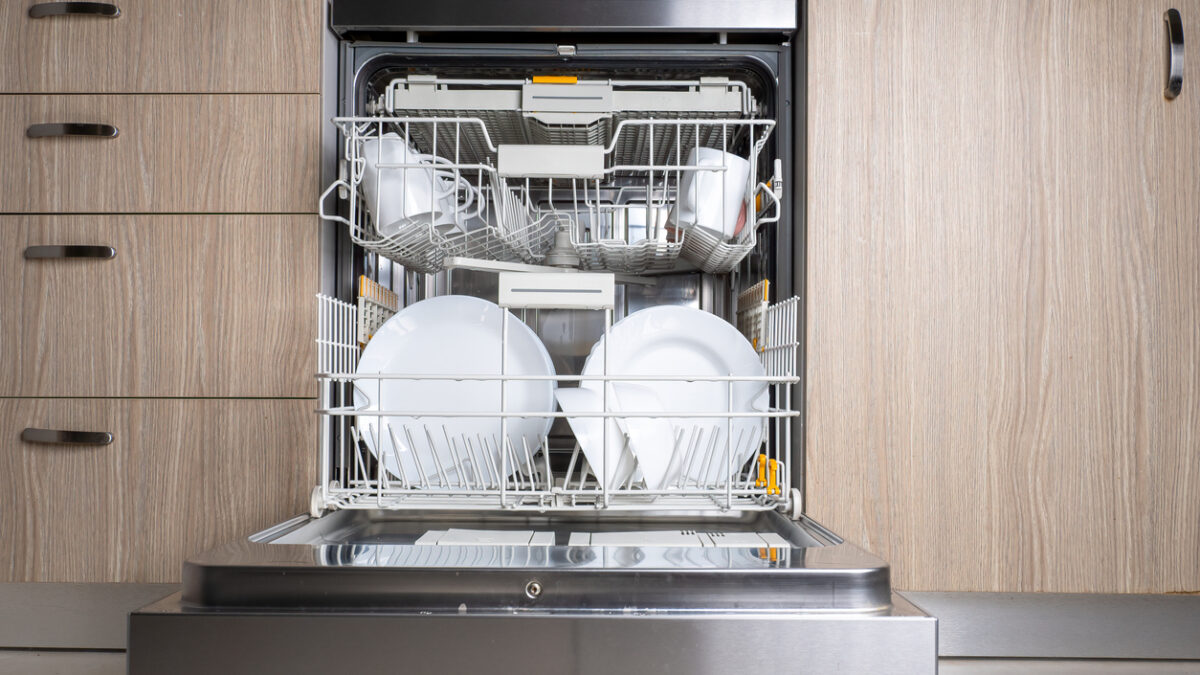 Open door of built in dishwasher. Kitchen with integrated appliances. Plates and dishes in the dishwasher.
